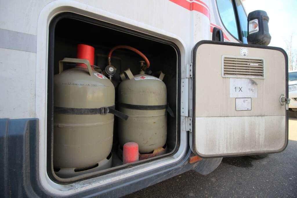 Open compartment of a vehicle containing two propane tanks with red caps.