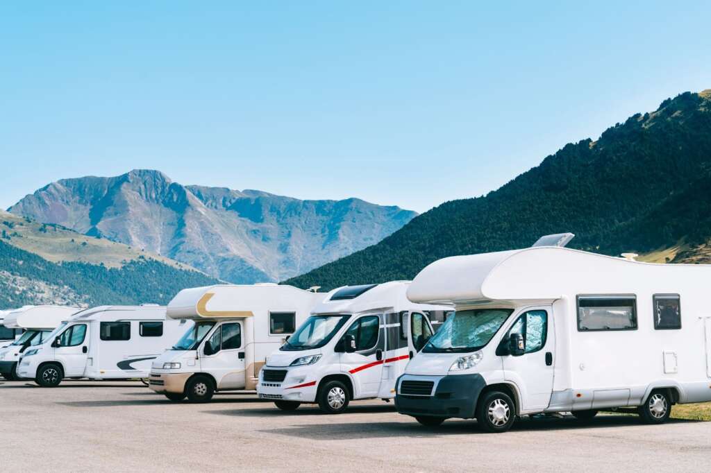 Row of white RVs parked with mountain backdrop.