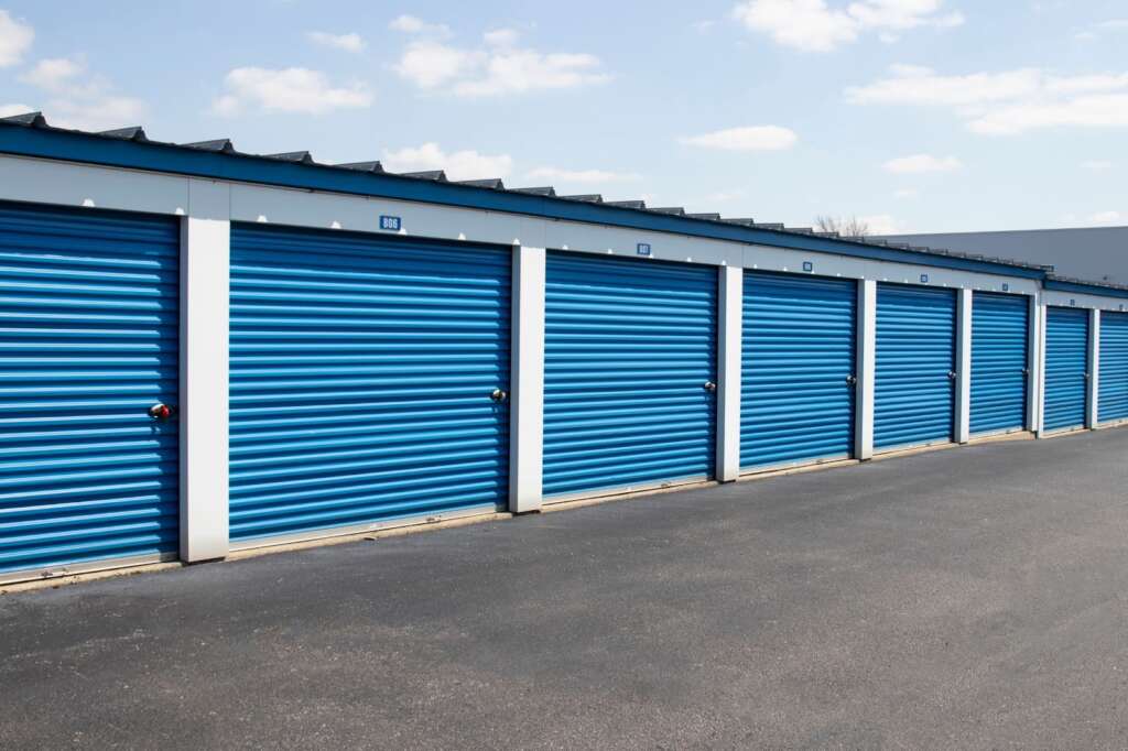 Row of blue storage unit doors with white frames under a partly cloudy sky.