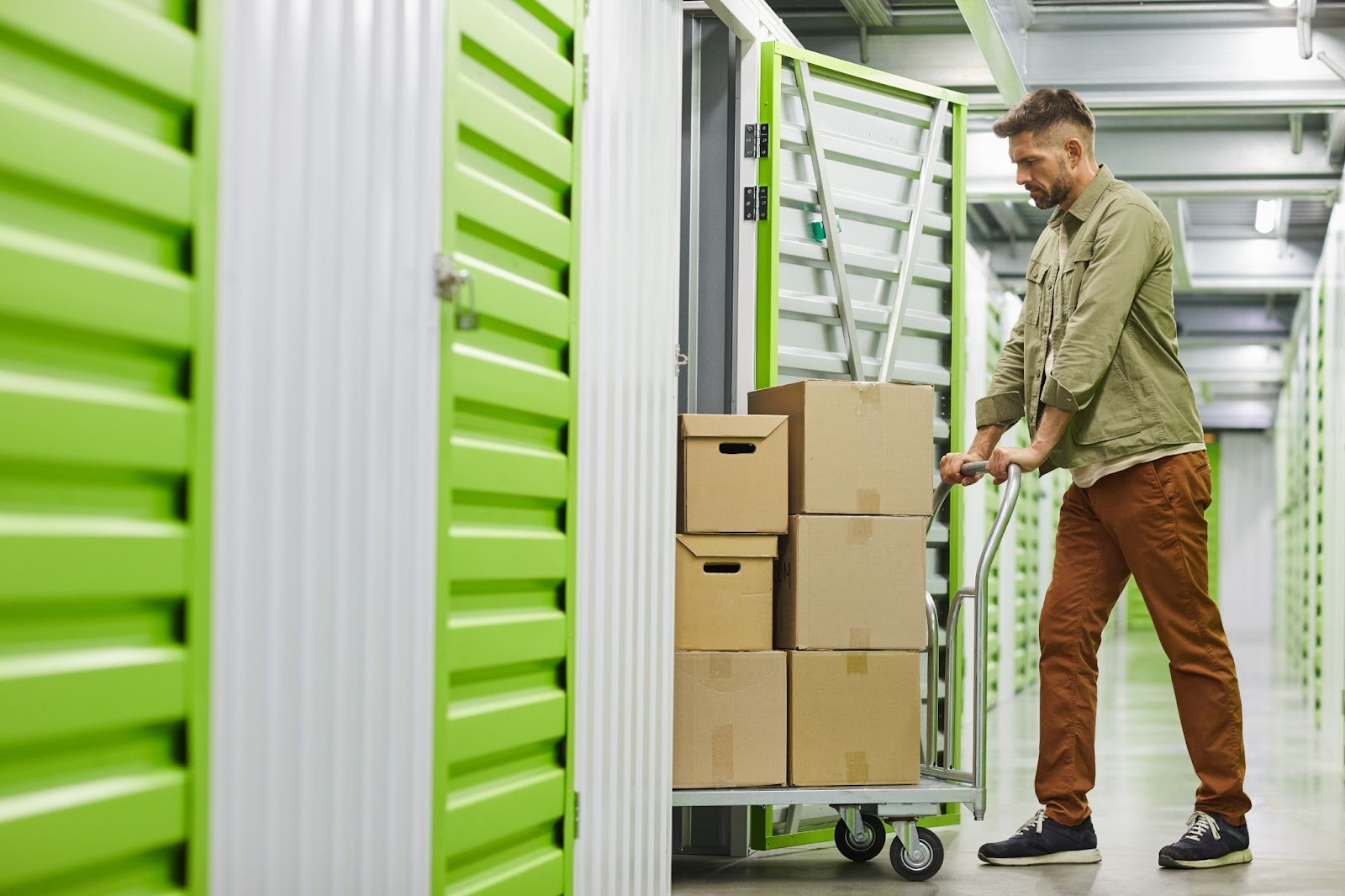 In a storage room, a man is pushing a cart loaded with various boxes.