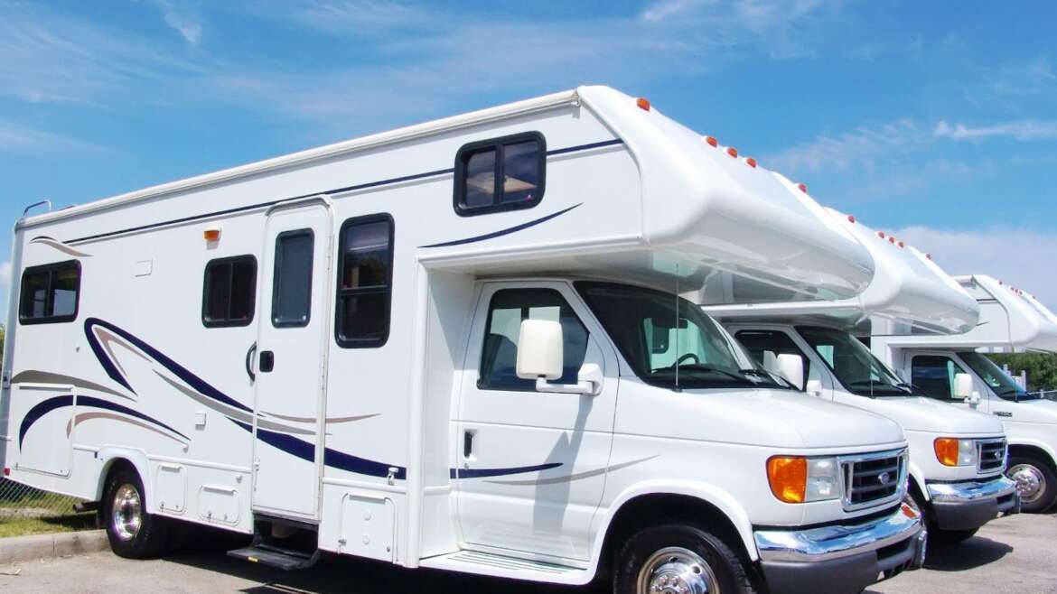 Three RVs parked in a spacious parking lot under clear blue skies