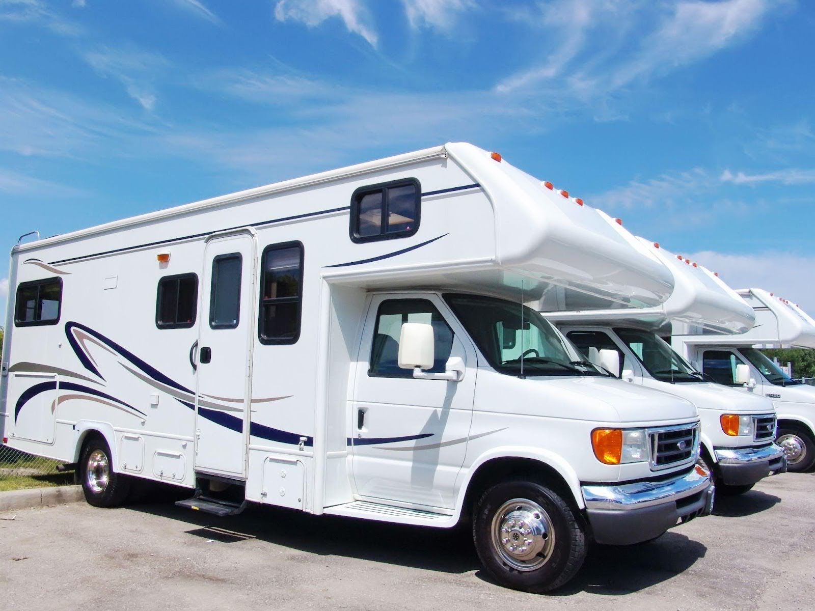 Three RVs parked in a spacious parking lot under clear blue skies