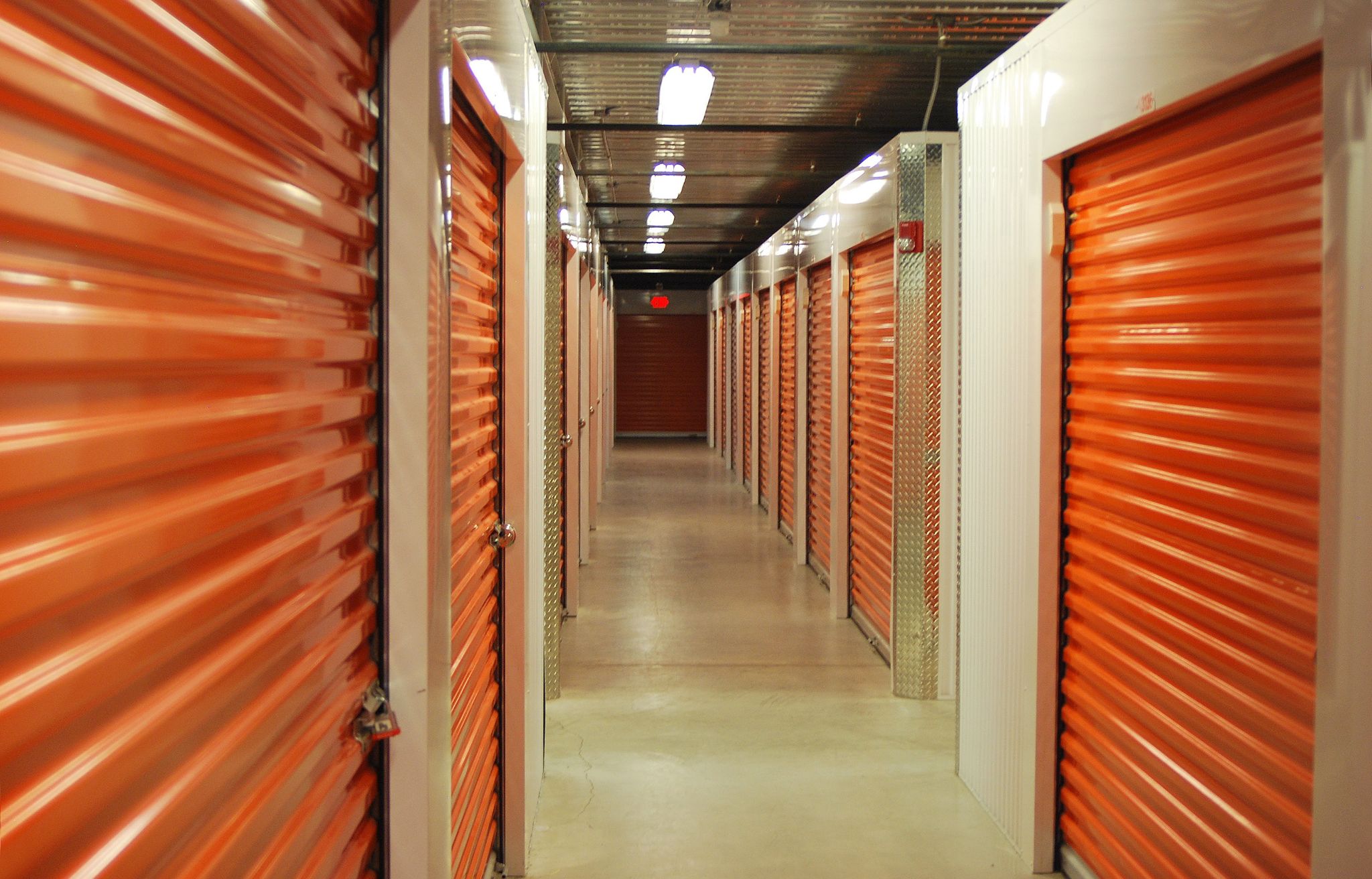 An indoor self-storage facility corridor with orange roll-up doors.