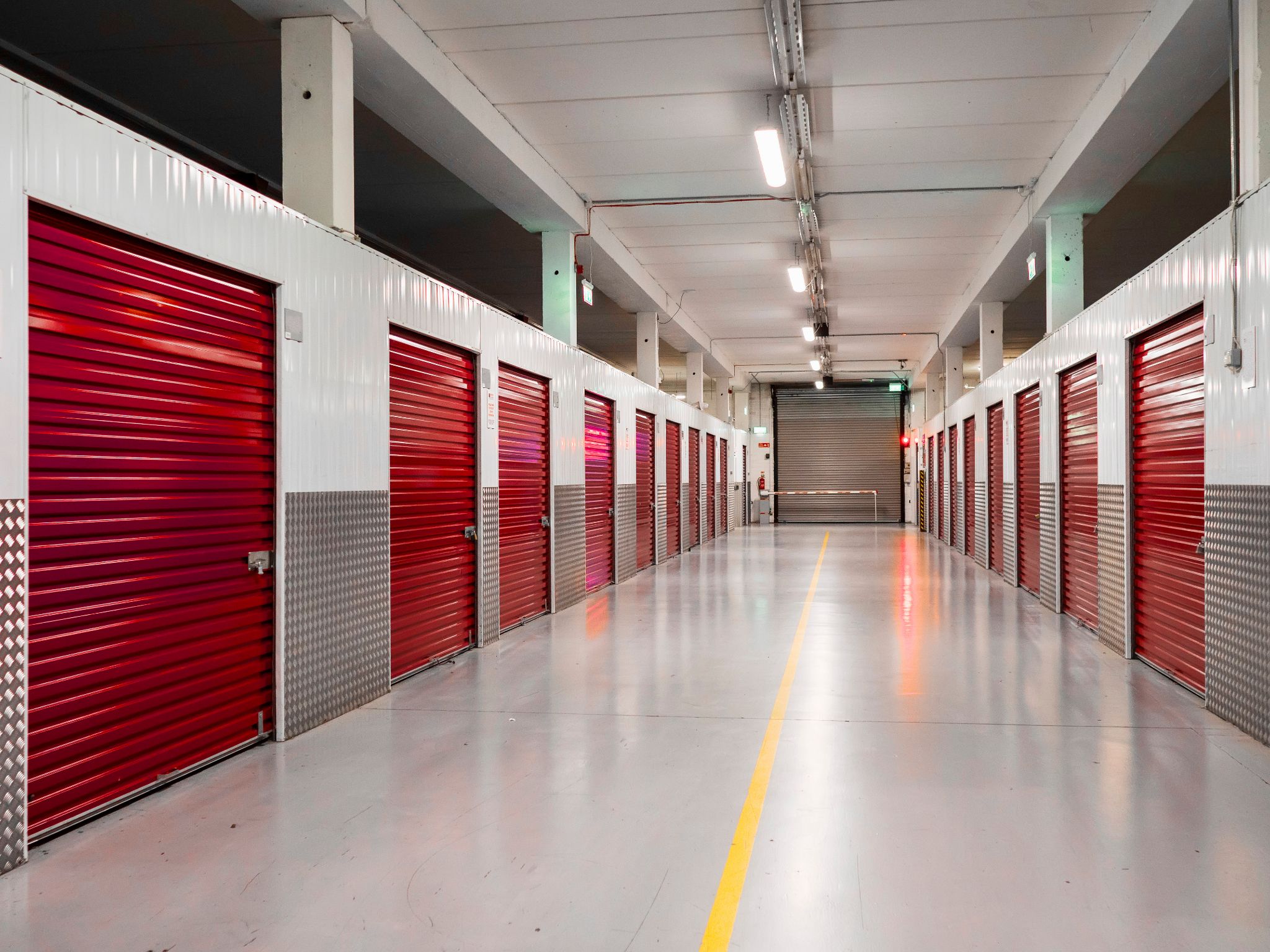 An indoor self-storage facility corridor with red roll-up doors.